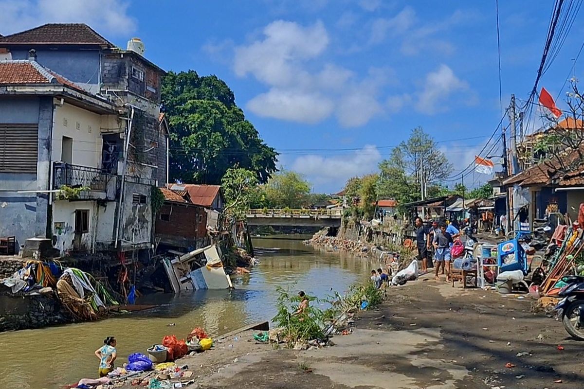 Warga yang tinggal di sekitar bantaran sungai Tukad Badung, Jalan Hasanudin, Kota Denpasar, Bali, tengah membersihkan sisa lumpur dam sampah pasca banjir, pada Kamis (11/8/2025). KOMPAS.com/ Yohanes Valdi Seriang Ginta