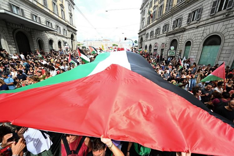 Orang-orang berbaris membawa bendera Palestina raksasa dalam aksi mogok nasional bertajuk Mari Blokir Semuanya sebagai bentuk solidaritas dengan warga Palestina di Gaza dan menyerukan penghentian pengiriman senjata ke Israel, di Roma pada 22 September. Serikat pekerja telah mengorganisir aksi mogok nasional 24 jam di seluruh sektor untuk menuntut pemerintah segera memutuskan hubungan dengan Negara Israel, sebagai bentuk solidaritas dengan rakyat Palestina dan Global Sumud Flotilla.
